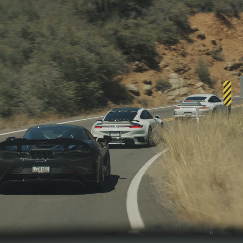 A grey McLaren 720S following a line of rally cars through a canyon curve.