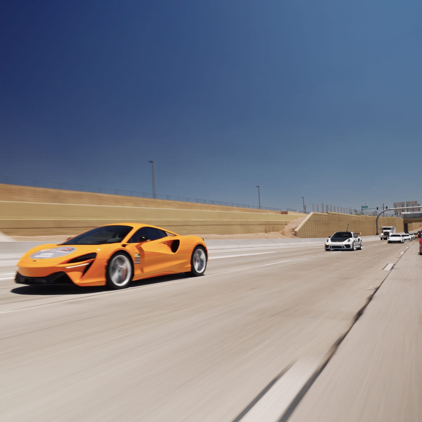 An orange McLaren GT leading a line of rally cars up the highway out of Scottsdale.