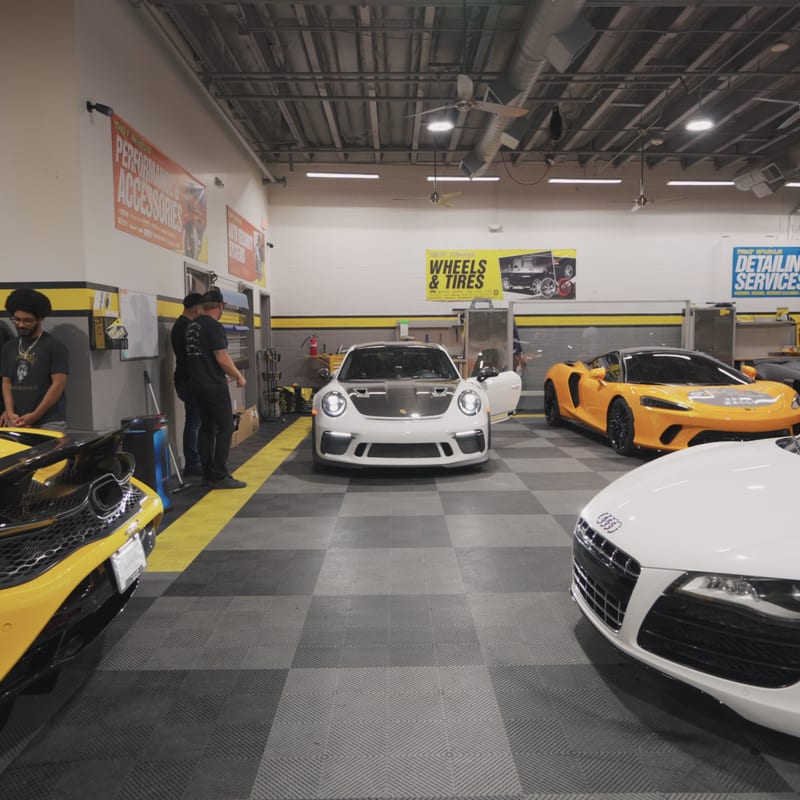 Rally cars lined up inside the launch venue, including a yellow McLaren, a white Porsche 911, and an Audi R8.
